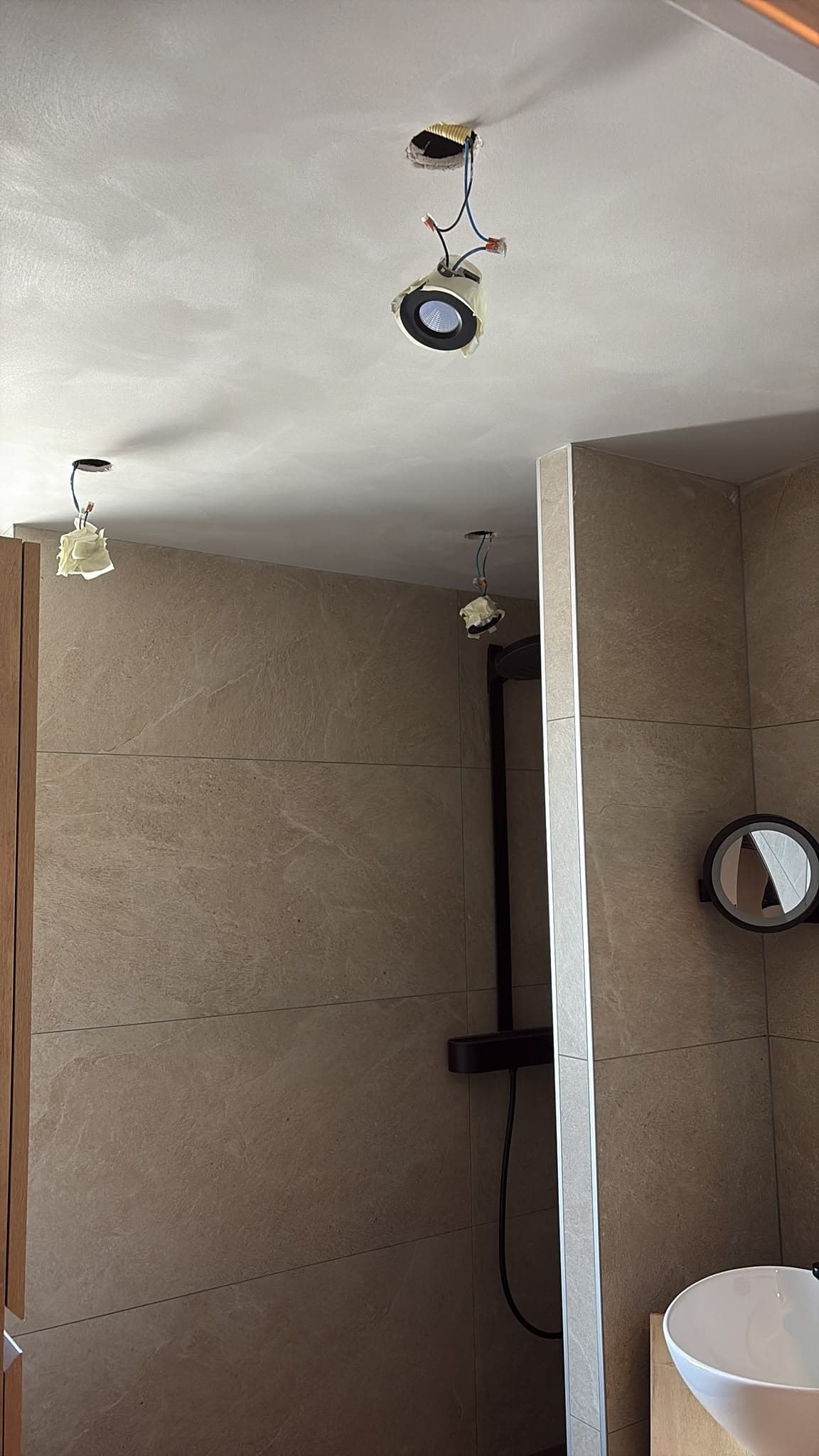 Detail van badkamerplafond met spots in aanleg, wastafel en spiegel zichtbaar